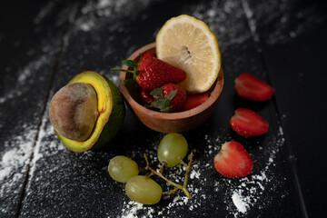 natural fresh red strawberries and half avocado and green grapes on black background with lemon slice