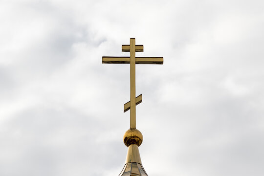 An Orthodox cross on top of the church dome against a cloudy cloudy sky.