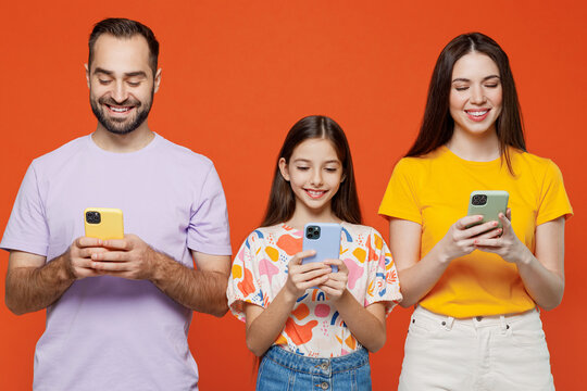 Young Fun Parents Mom Dad With Child Kid Daughter Teen Girl In Basic T-shirts Hold In Hand Use Mobile Cell Phone Isolated On Yellow Background Studio Portrait Family Day Parenthood Childhood Concept