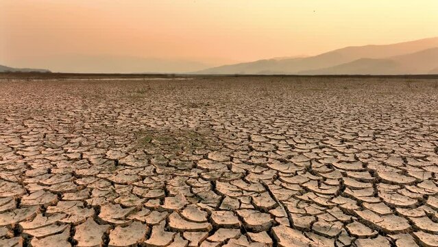 Drought and climate change, Landscape of cracked earth with orange sky after Lake drying on summer. Water crisis an impact of global warming.