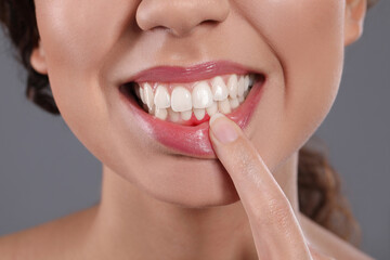 Young woman showing inflamed gums on grey background, closeup