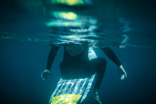 underwater photo of a half-sunken surfer on his board seen from behind