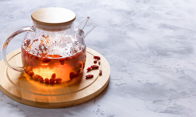Glass teapot with hot tea with goji berries on a bamboo stand. Selective focus.