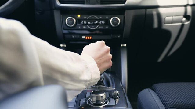 Close up of a unrecognizable business woman hand in white casual clothes at the wheel of a car, shifting gears in auto. European girl drives an automobile.