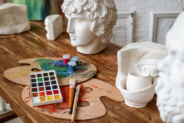 Painter wooden workplace with palettes, brushes, watercolor set and plaster apollo head model