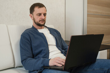 The concept of remote freelance work. A man is typing on a laptop while sitting on the couch at home.