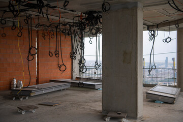 interior of skyscraper floor under construction. Cables, pipes and tubes hanging from ceiling of room. Building under construction, work in progress. Placement of electrical wires and cables.