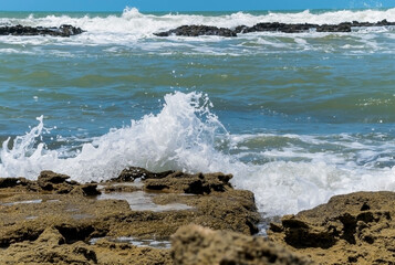 Grandes pedras escuras com ondas batendo em volta, com o mar ao fundo localizada Cabrália, Bahia