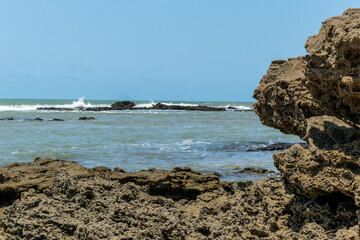 Linda praia com grandes pedras escuras e ondas em volta, com o mar ao fundo localizada Cabrália Bahia