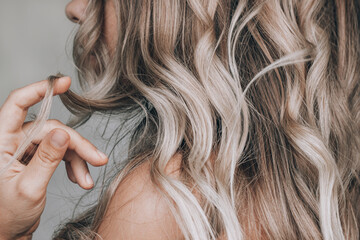 A young blonde woman with the wavy hair holding a lock of hair in her hand isolated on a gray...