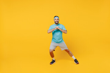 Fototapeta na wymiar Full body fun young fitness trainer instructor sporty man sportsman in headband blue t-shirt spend weekend in home gym do lunges isolated on plain yellow background. Workout sport motivation concept.
