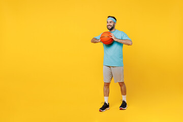 Fototapeta na wymiar Full body fun young fitness trainer instructor sporty man sportsman in headband blue t-shirt spend leisure time in gym throw basketball ball isolated on plain yellow background. Workout sport concept.