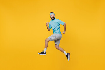 Full size side view strong young fitness trainer instructor sporty man sportsman wear headband blue t-shirt jump high run fast look aside isolated on plain yellow background. Workout sport concept