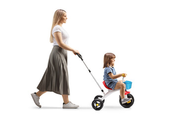 Full length profile shot of a mother pushing a girl on a tricycle