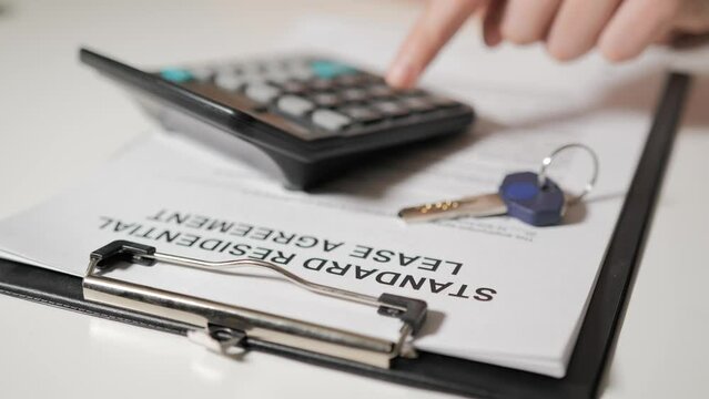 Standard tenancy agreement. The hands of realtor calculate the cost on calculator. In the foreground lies the key to the apartment or house.
