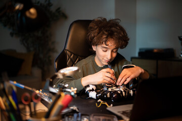 The boy spends time at home at desk digging into the electronics that power the robot, pulls out wires with a tweezers and solders them tutorial instructions in laptop