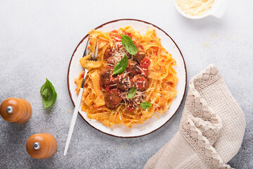 Tagliatelle pasta with meatballs in tomato sauce and thyme in sauce on light grey slate, stone or concrete background. Traditional Italian dish and cuisine. Top view with copy space.