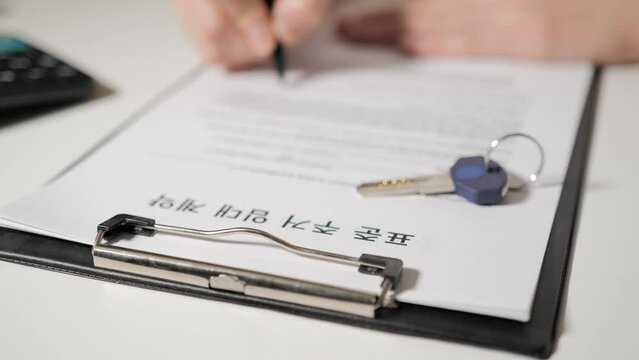 Standard Residential Lease Agreement in Korean speaking language. Female or male hands sign documents. In the foreground lies the key to the apartment or house.