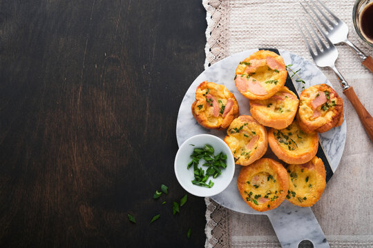 Delicious egg muffins with green onions, bacon, cheese and tomatoes on wooden board on old wooden rustic background. Healthy high protein and low carb breakfast. Homemade food.
