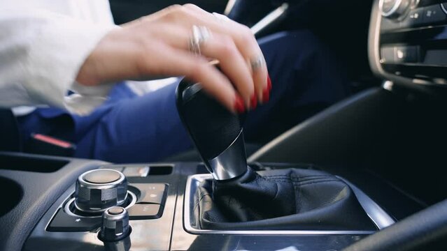 Business Woman controls auto and switch gears, turn on. A hand of driver girl is shifting the automatic gear in car close up. Female driving and changing gear on a beautiful sunny day.