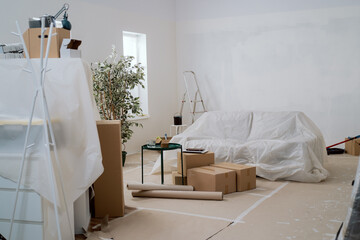 Interior of the room during renovation painting walls with ladder, floor and couch protected with...