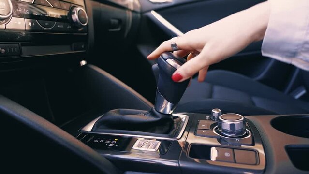 Hand of businesswoman use gear stick, change, shifting the automatic transmission in luxury gray car close up inside view at evening sunny.