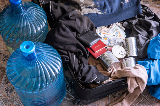 Clothes, canned food, money and documents are in a suitcase. Concept - collection of things during a natural disaster, emergency, quick evacuation during a disaster. Drinking water bottles.