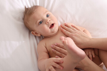 Mother massaging her cute baby with oil on bed, closeup