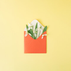 Snowdrops flowers in a red letter envelope on a yellow background. Minimal spring flatlay.