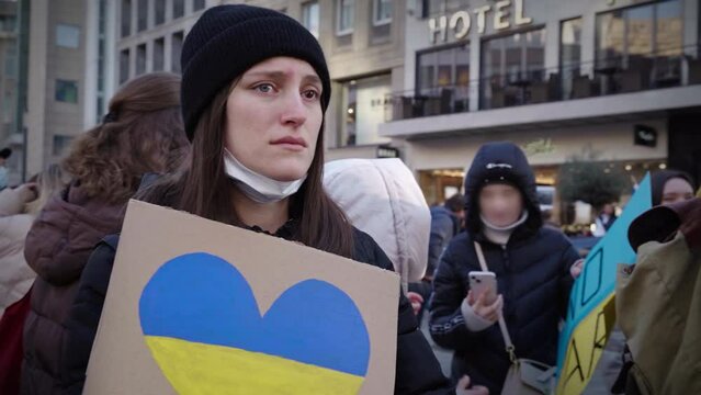 A pretty young Ukrainian woman holds a cardboard with the Ukrainian flag in the shape of a heart. She protests crying against the war in Ukraine. (2)