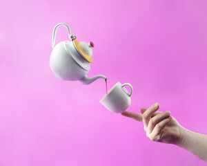 Teapot and tea cup standing on a finger on a purple background. Minimal composition layout