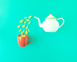 A white teapot pours rose petals into a red cup on a turquoise blue background. Minimal flat lay composition.