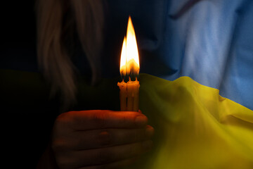 The girl is holding a candle and praying for Ukraine against the background of the flag of Ukraine, we all grieve and pray for peace, vryna in Ukraine, a hand with a candle,