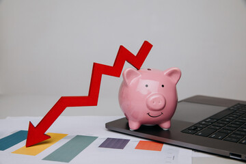 Pink piggy bank and red arrow down graphic in office, problem in business