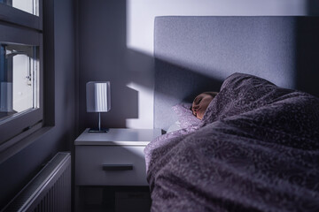 Sleeping woman in bed at night in dark bedroom. Person resting. Asleep under cover and blanket....
