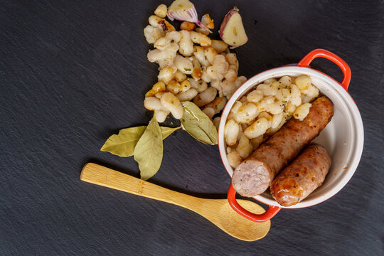 Sausages with white beans, in catalan butifarra with mongetes, typical dish from catalonia, spain. slate plate and wooden spoon.