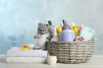 Wicker basket with different baby cosmetic products, towel and toys on white wooden table
