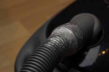 Closeup of a broken vacuum cleaner with a hose fixed with a duct tape.