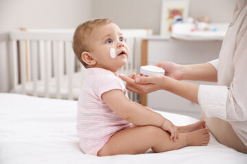 Mother applying moisturizing cream on her little baby at home, closeup