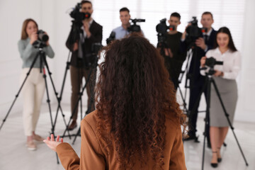 African American business woman talking to group of journalists indoors, back view
