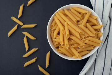 A bowl of raw pasta on a dark background. Scattered pasta and a dishcloth. 