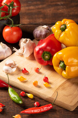 Table with red and yellow peppers, peppers, onions and garlic and tomatoes, over rustic wood, black background, selective focus.