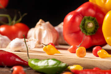 Table with red and yellow peppers, peppers, onions and garlic and tomatoes, over rustic wood, black background, selective focus.