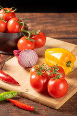Table with red and yellow peppers, peppers, onions and garlic and tomatoes, over rustic wood, black background, selective focus.