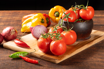 Table with red and yellow peppers, peppers, onions and garlic and tomatoes, over rustic wood, black background, selective focus.