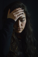 Portrait of a beautiful young woman with long hair who with one hand on her forehead looks sad and desperate