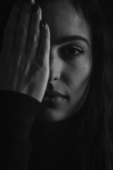 Close up portrait in black and white of a beautiful young woman who with one hand hides half of her face