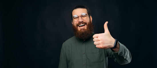 Ecstatic bearded man is showing like gesture over black background.
