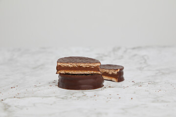Three dark chocolate and dulce de leche alfajores on a marble table.