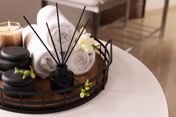 Aromatic reed air freshener, rolled towels, spa stones and candle on white table indoors